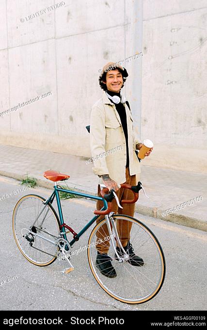 Smiling man holding bicycle handlebar while standing on footpath
