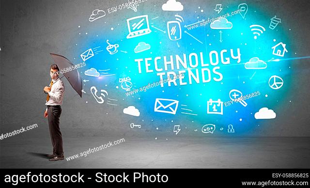 Businessman defending with umbrella from TECHNOLOGY TRENDS inscription, modern technology concept