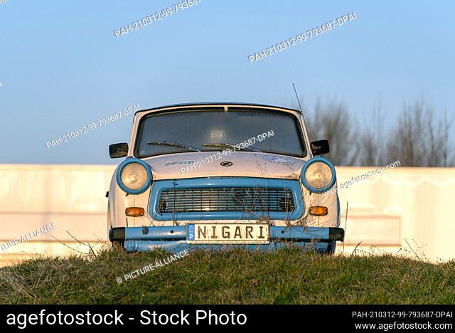 08 March 2021, Saxony-Anhalt, Magdeburg: An old Trabant in the colours of the football club 1. FC Magdeburg stands on a hill at sunrise