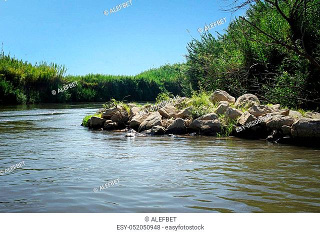 View of the slow river flow and the bushes growing along the banks of the Jordan River, Israel