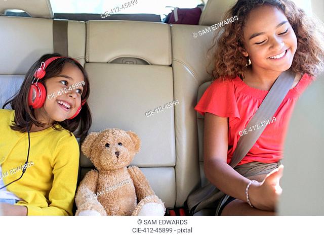 Happy sisters and teddy bear riding in back seat of car