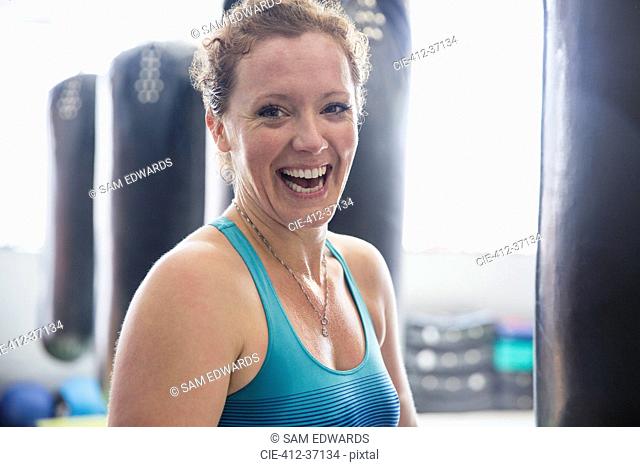 Portrait laughing female boxer standing at punching bag in gym