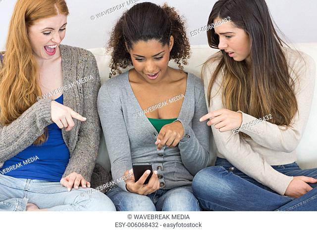 Female friends pointing at mobile phone together on sofa