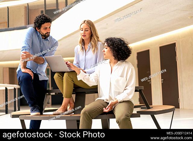 Businesswoman discussing over laptop with colleagues at office corridor