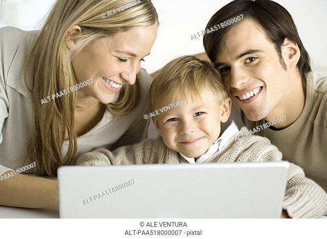 Family gathered around laptop computer, father and son smiling at camera