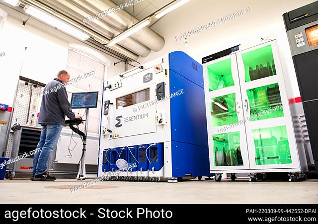 PRODUCTION - 24 February 2022, Schleswig-Holstein, Neumünster: Carsten Wolfgramm, Deutsche Bahn 3D printer, stands in front of a 3D printer (l) and a dryer (r)...