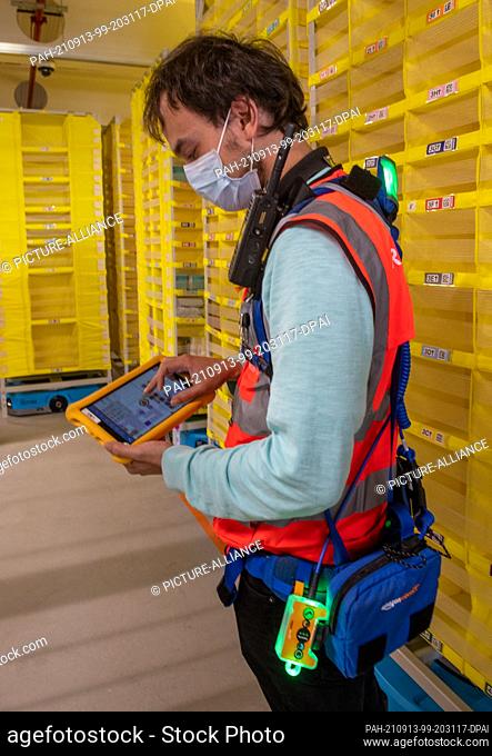 13 September 2021, Bavaria, Graben: Philipp Weiß controls logistics robots at the Amazon company with a tablet. The logistics center in the district of Augsburg...
