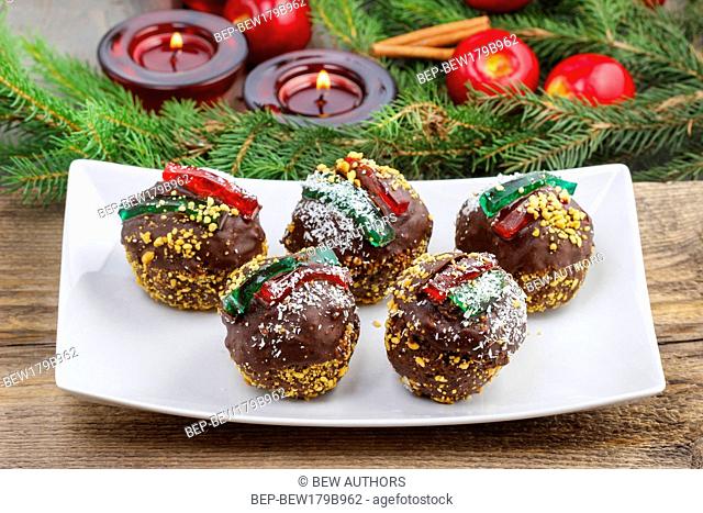 Round shape chocolate christmas cakes, decorated with jelly strips, nuts and coconut. Christmas tree, apples and lanterns in the background