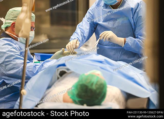 PRODUCTION - 29 November 2023, Schleswig-Holstein, Rendsburg: A surgical nurse (r) hands a pair of scissors to the surgeon during an operation in the Schön...