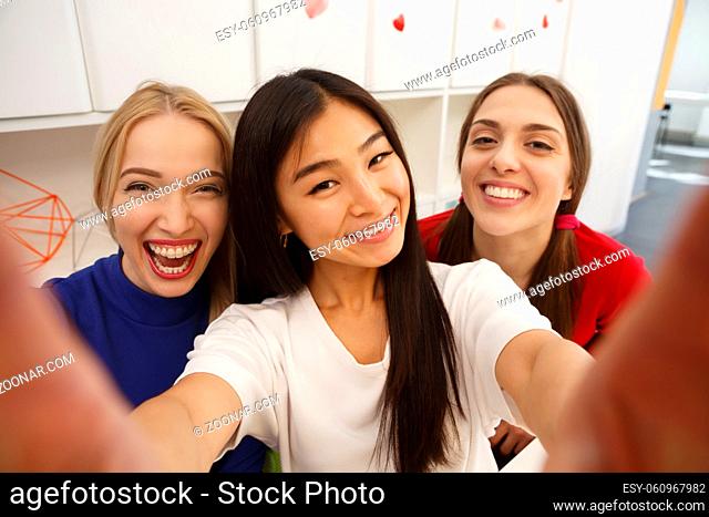 Portrait of happy students making selfies in library while studying. Beautiful ladies photographing for their foreign friends