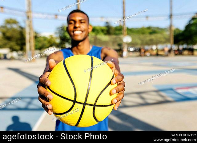 Smiling man holding yellow basketball at sports court