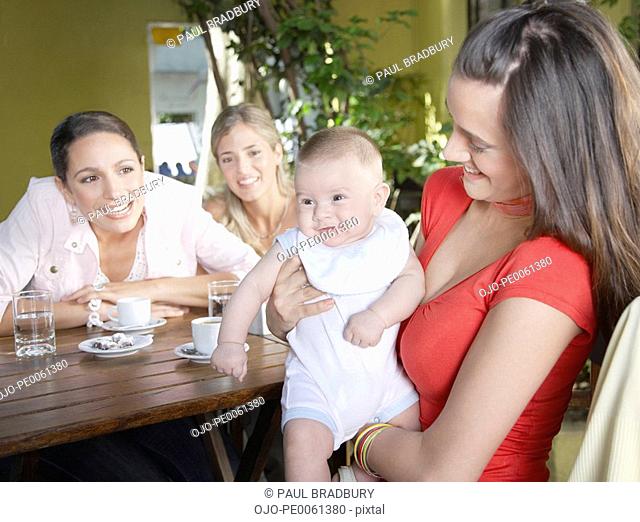 Three women on outdoor patio where one is holding a smiling baby