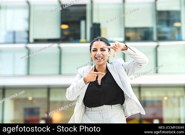 Cheerful businesswoman showing finger frame in city