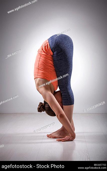 Sporty fit woman practices bending yoga asana Uttanasana, standing forward bend pose