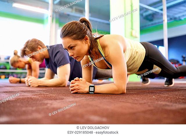 fitness, sport, exercising and people concept - woman with heart-rate tracker at group training doing plank exercise in gym