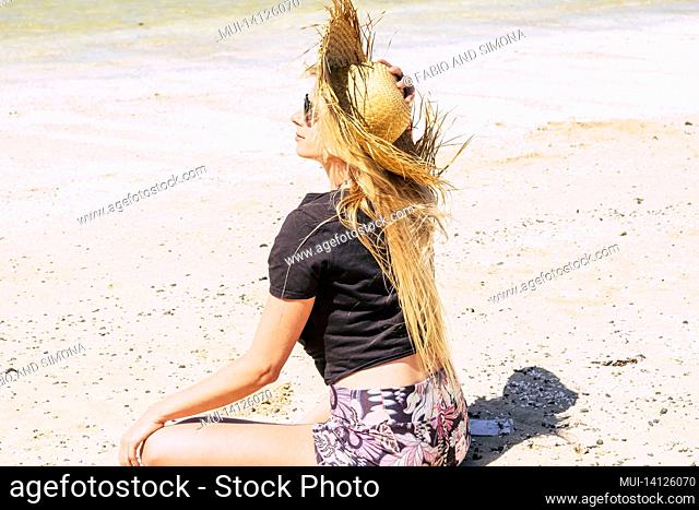 beautiful woman in straw hat relaxing on sand at beach on a bright sunny day during summer. woman relaxing while holidaying on sandy beach during summertime