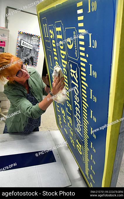 23 June 2021, Saxony, Penig: At Muldenthaler Emallierwerk GmbH, the head of the sign department, Katrin Engert-Hecht produces signs using the hand screen...