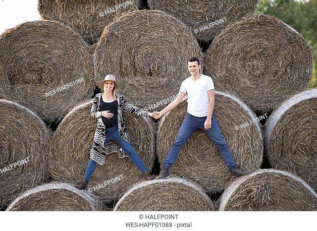Happy expectant parents standing on bales of straw