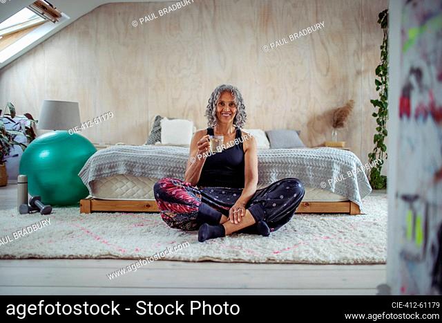 Portrait happy senior woman drinking water on bedroom floor