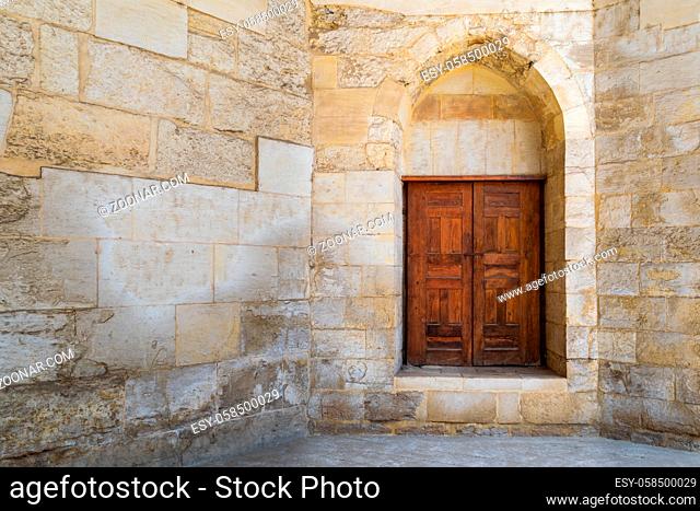 Vaulted closed decorated wooden grunge door in bricks stone wall at public historic Amir Aqsunqur Mosque, Blue Mosque, Cairo, Egypt