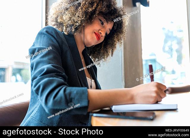 Afro businesswoman writing in diary at coffee shop