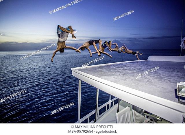 five men are jumping synchronically with backflip from boat