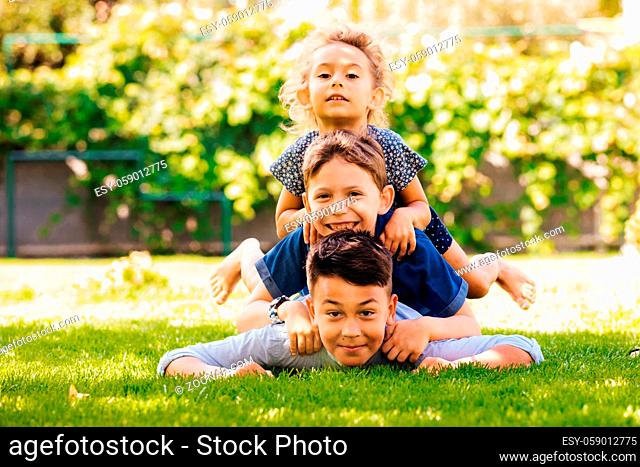Portrait of three little children as a tower on a green grass. Playful siblings at the backyard