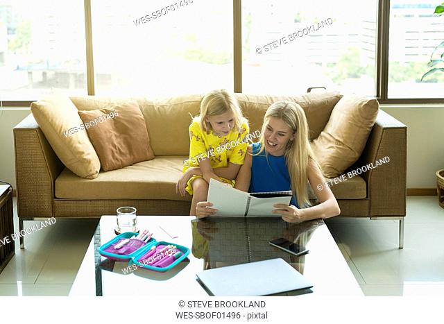 Happy mother and daughter sitting on a couch looking at the girl's homework together
