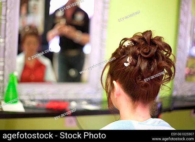 Hairdresser doing a woman's hair in professional hairdressing salon or barbershop , seen from behind the customer, unrecognizable