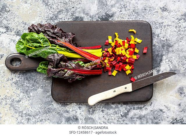 Brightly coloured swiss chard sliced on a wooden board with a knife