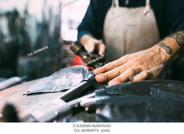 Hands of metalworker hammering lead metal in forge workshop