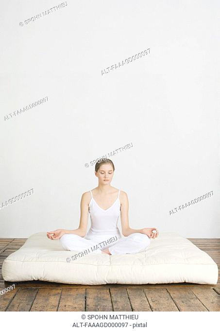 Young woman sitting in lotus position on futon mattress