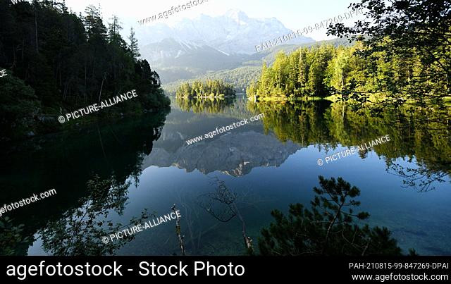 15 August 2021, Bavaria, Grainau: The Zugspitze (M) is reflected in the still smooth surface of the Eibsee. Photo: Angelika Warmuth/dpa