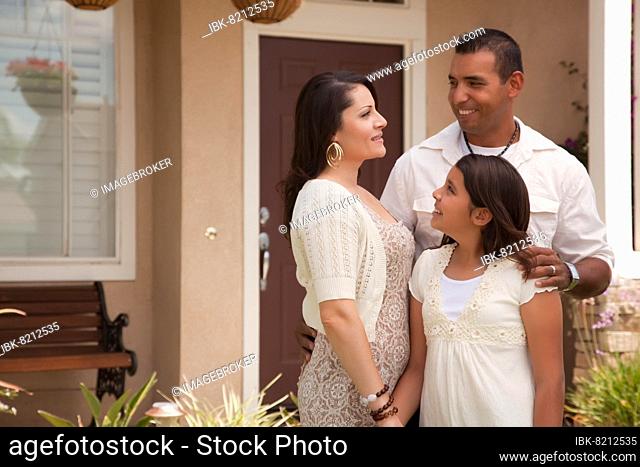 Small hispanic mother, father and daughter in front of their home