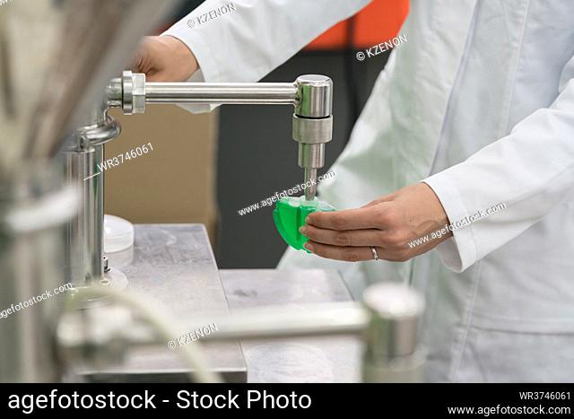 Side view close-up of the hand of a female technician, filling a plastic container with liquid substance for laboratory tests during quality control in a...