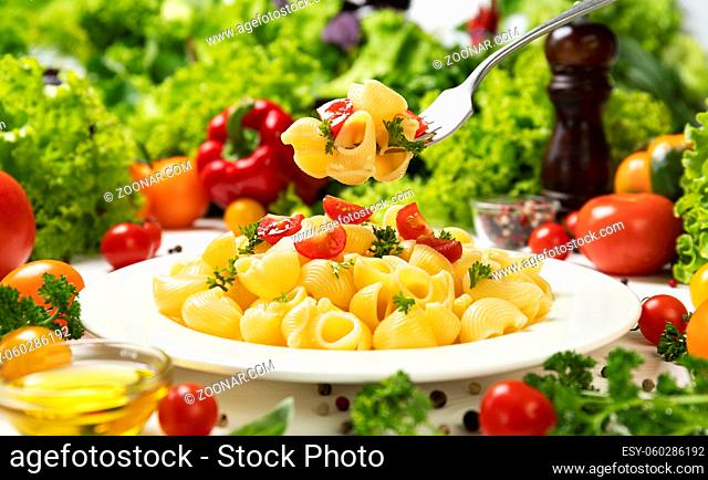 Plate of cooked italian pasta, pipe rigate on fork with tomatoes and basil leaves