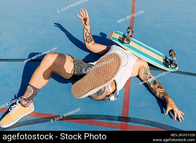 Fallen young man with skateboard on face at basketball court during sunny day