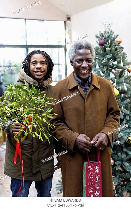 Portrait smiling grandfather and grandson arriving with Christmas gift and mistletoe