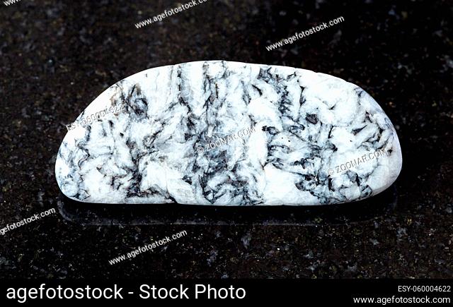 closeup of sample of natural mineral from geological collection - rolled Magnesite rock on black granite background from Satkinskoe deposit, Southern Urals