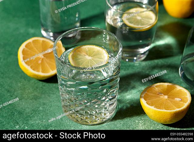 glasses with water and lemons on green background