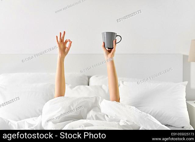 woman with cup of coffee lying in bed showing ok