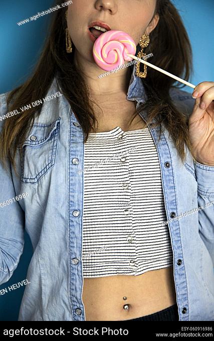 Portrait of a beautiful girl with colorful pink twirl lollipop hard candy on blue background, sweets, sugar and unhealthy food concept beauty