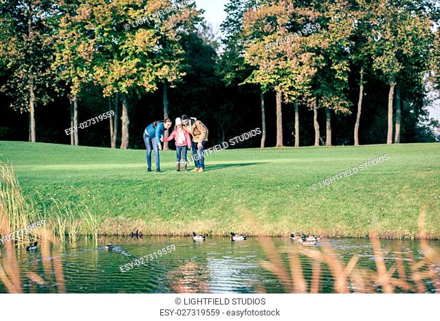 Happy family with one child looking at ducks near beautiful lake in autumn park
