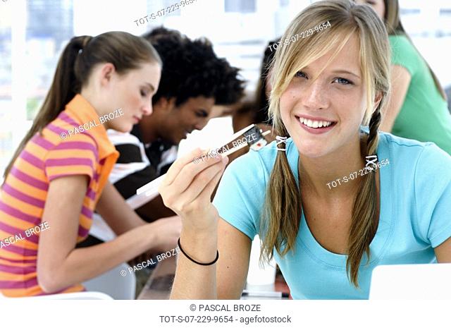 Portrait of a teenage girl holding chopsticks and smiling with her friends sitting in the background