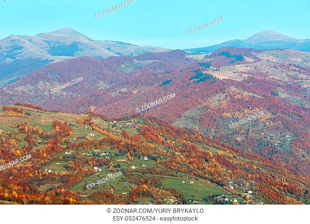 Autumn Carpathian Mountains landscape with multicolored trees on slope, village, Goverla and Petros mountains in far (view from Rakhiv pass, Transcarpathia