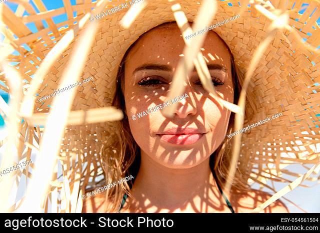 Front view of a Caucasian woman wearing a straw hat, reclining on the beach and sunbathing. Weekend beach vacation, lifestyle and leisure