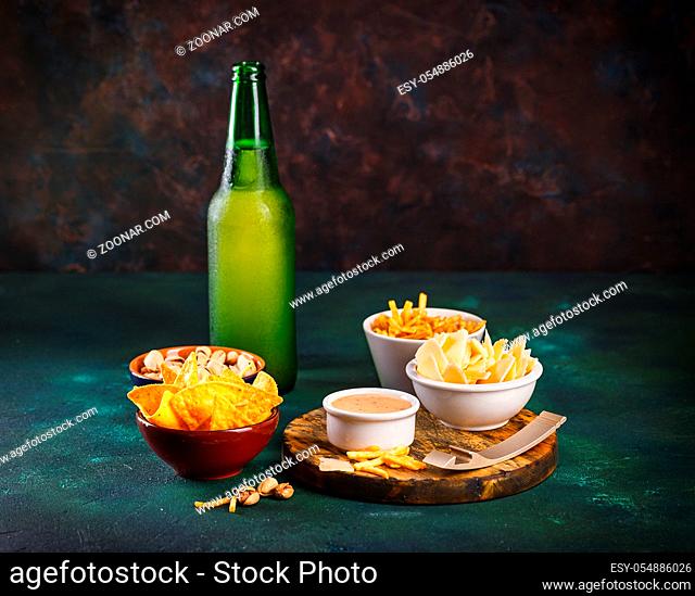 Glass mug with beer with foam and water drops and snacks on a dark green background