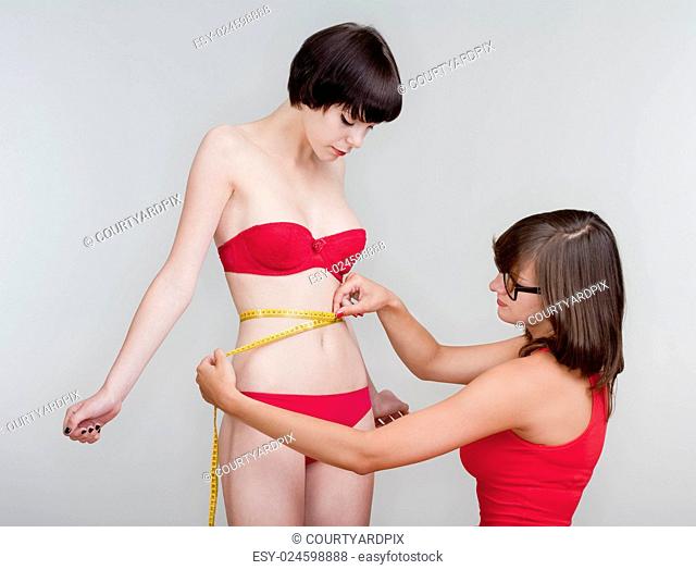 two young female friends measuring results of diet - isolated on gray