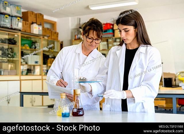 Mature female scientist with document examining chemical with colleague at laboratory