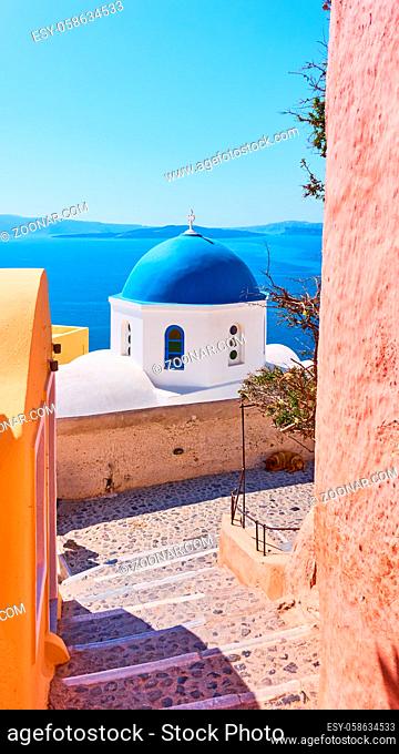 Street and Greek orthodox church with blue dome by the sea in Oia town in Santorini island, Greece